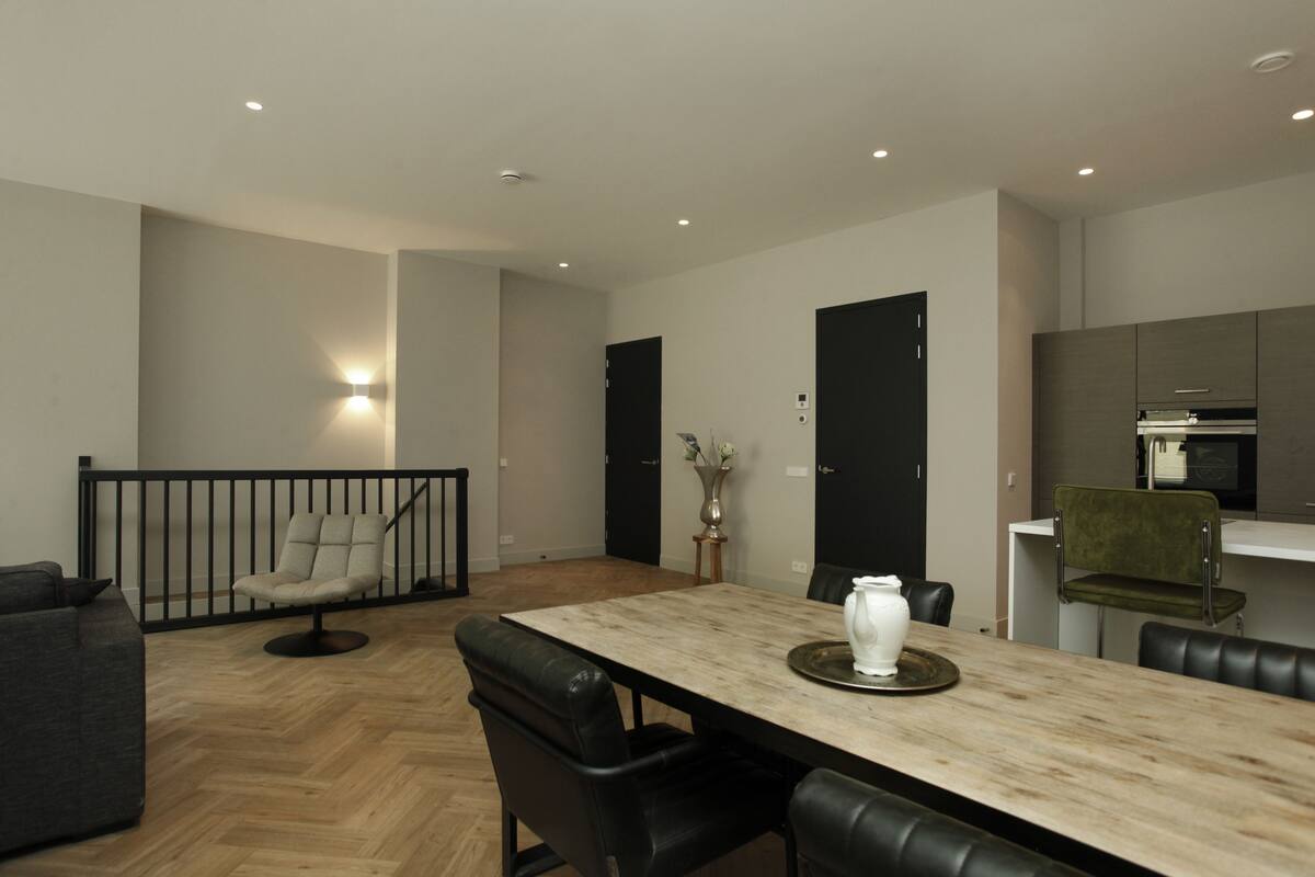 Un espace repas moderne avec une table en bois, des chaises en cuir noir et une rambarde noire.
