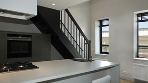 Una cocina moderna con una isla central, horno integrado y una escalera negra.