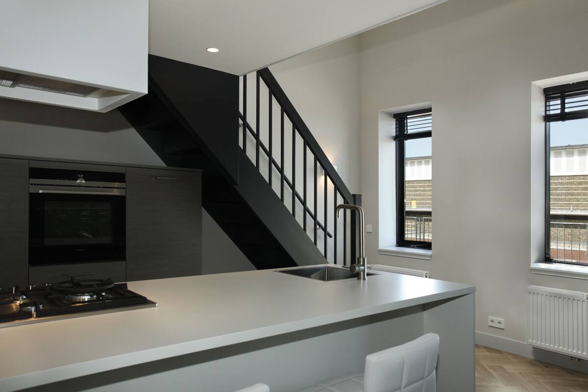Une cuisine moderne dotée d’un îlot central, d’un four encastré et d’un escalier noir.