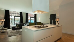 Una cocina moderna con una isla central, un comedor con sofá y sillas, y vistas de la ciudad a través de amplias ventanas.