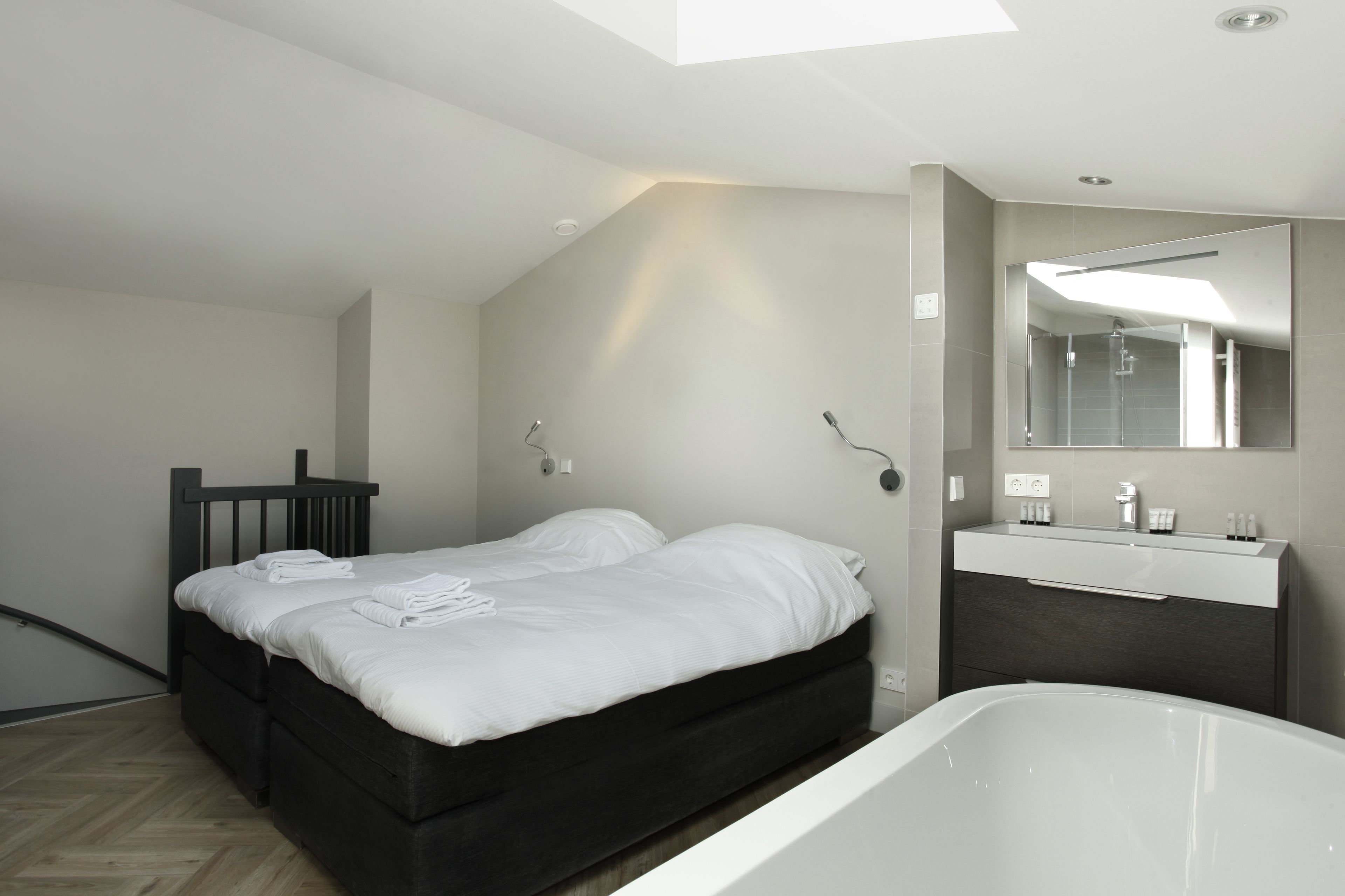 A modern bedroom with a large bed, a built-in vanity, and a bathtub.