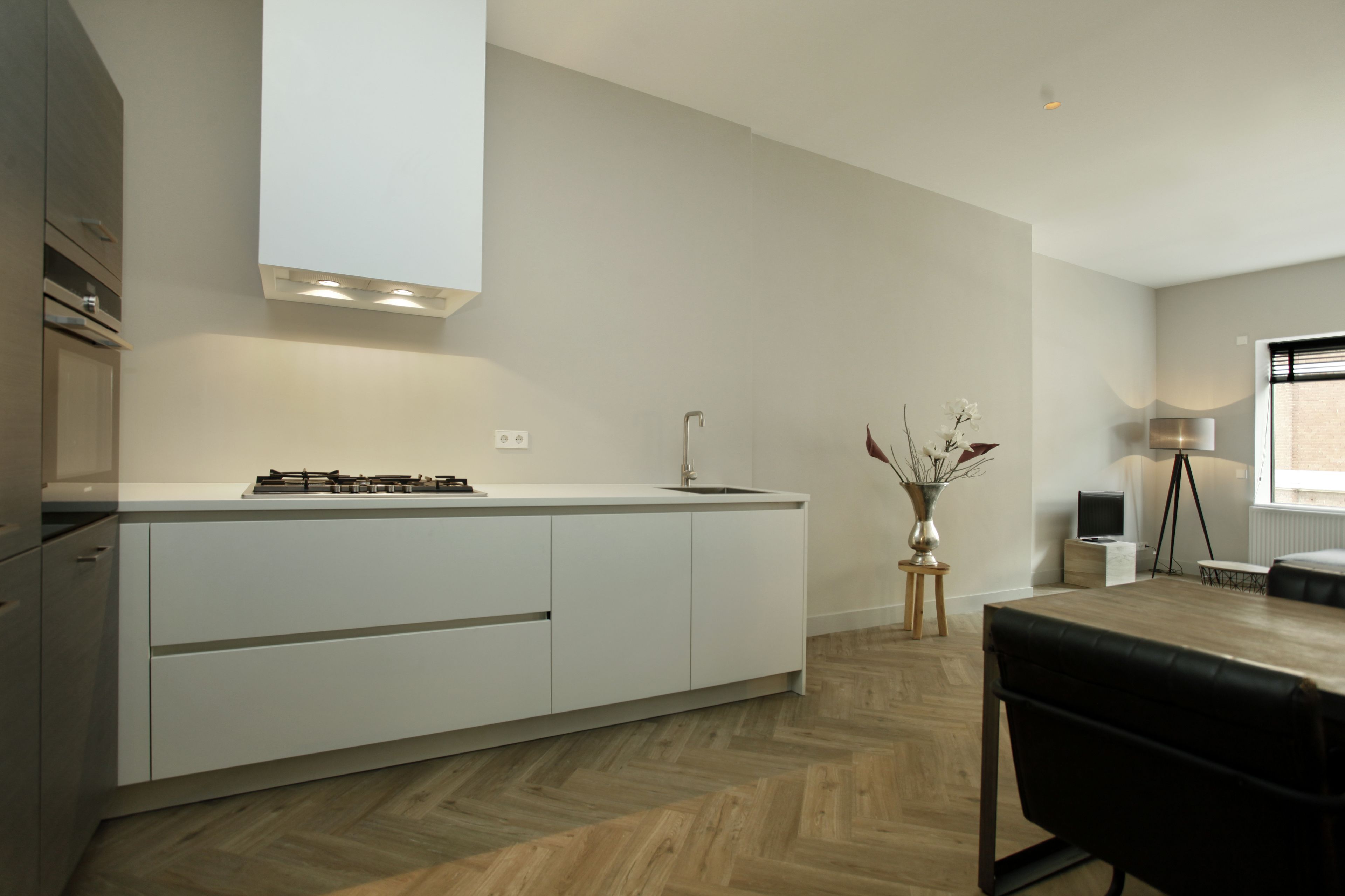 Une cuisine moderne avec des meubles blancs, une cuisinière à gaz et un plancher en bois disposé en motif «arête de poisson».