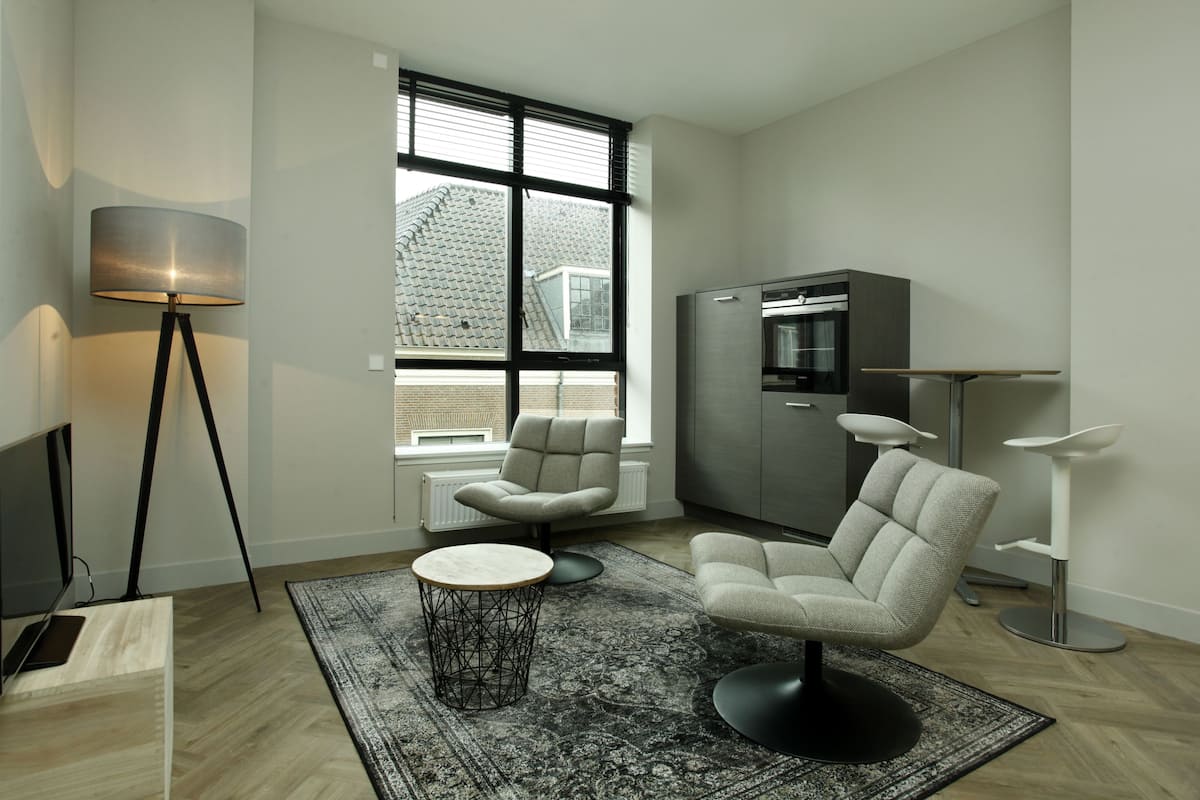 Un salon moderne avec une grande fenêtre, un canapé, une table basse, un lampadaire et un téléviseur.