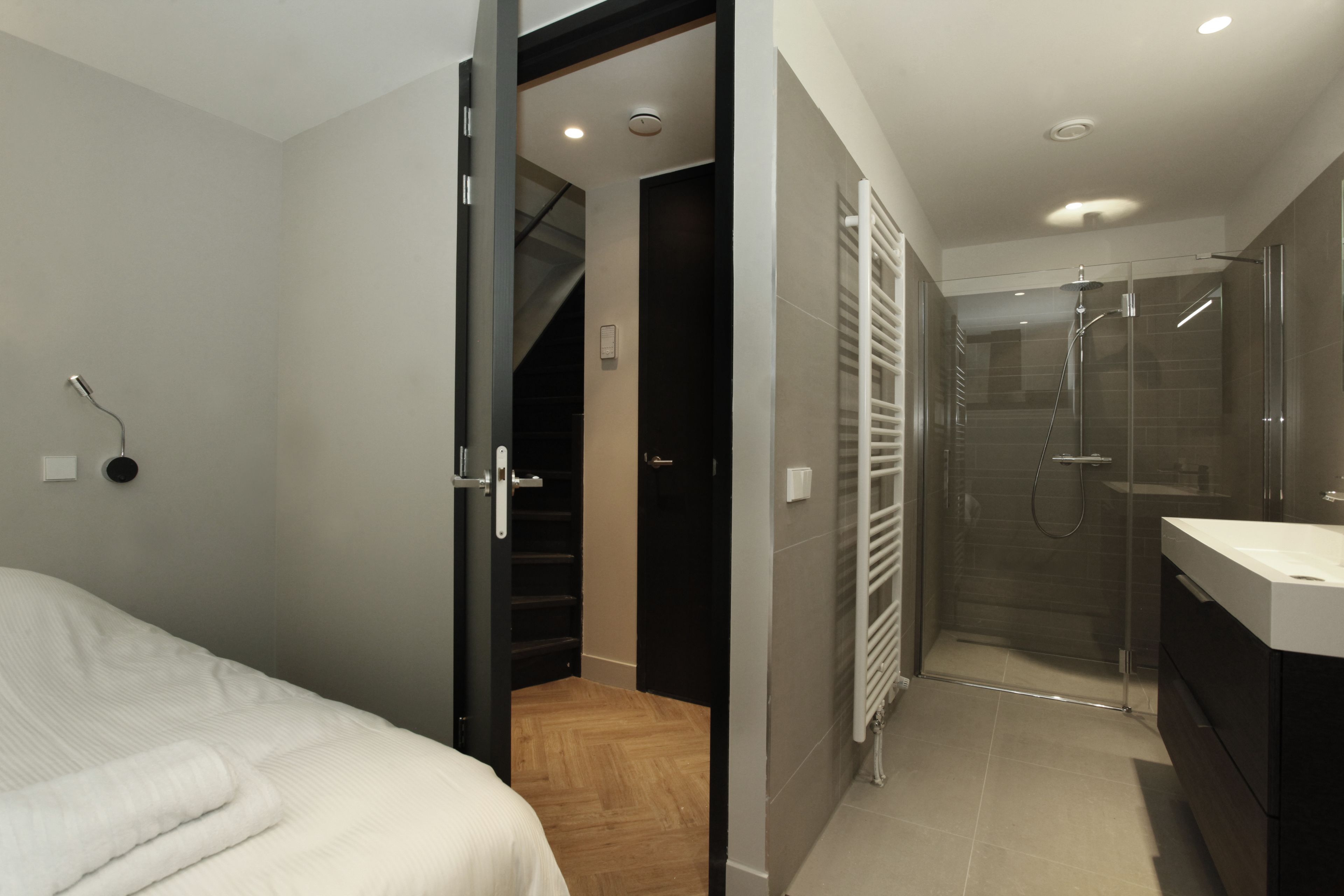 A modern bathroom with a glass shower, a white sink, and a wooden floor.