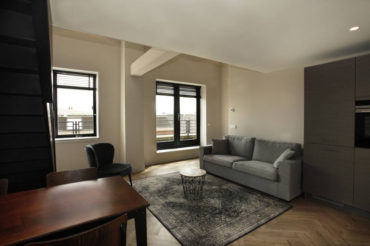 Un salon moderne avec un canapé gris, une table à manger en bois et un tapis à motifs.