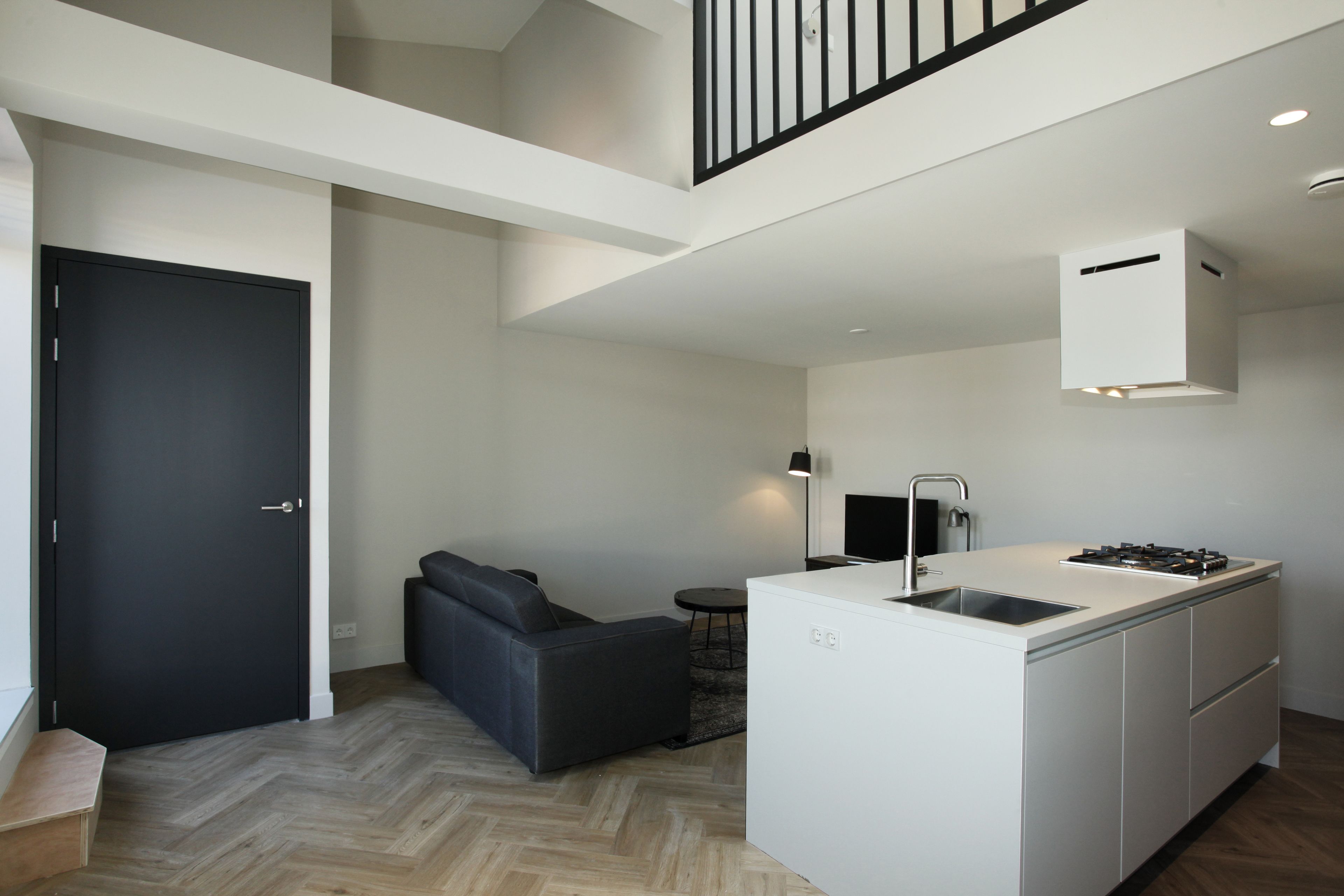 A modern kitchen with a built-in island, a dark-colored sofa, and a staircase leading to an upper level.