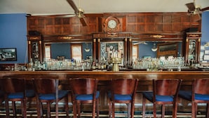A bar with wooden bar tops, a clock, and multiple bottles. - The Hotel Belvidere (Hawley)