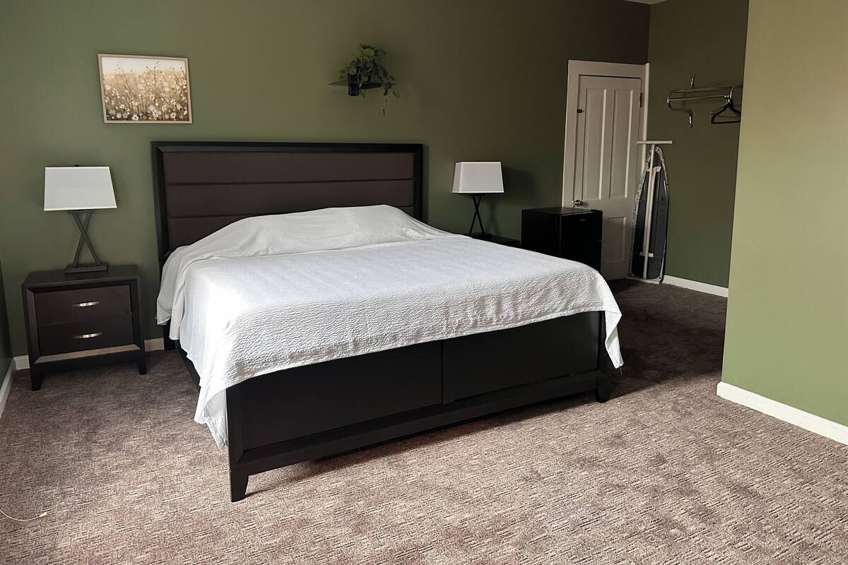 A bedroom with a bed, two bedside tables with lamps, a door, and a coat rack.