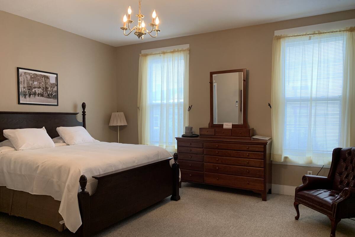 A bedroom with a large bed, a dresser, a chair, and a chandelier.