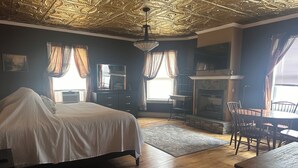 A room with a bed, a fireplace, a dining table with chairs, and a ceiling with intricate patterns. - The Hotel Belvidere (Hawley)