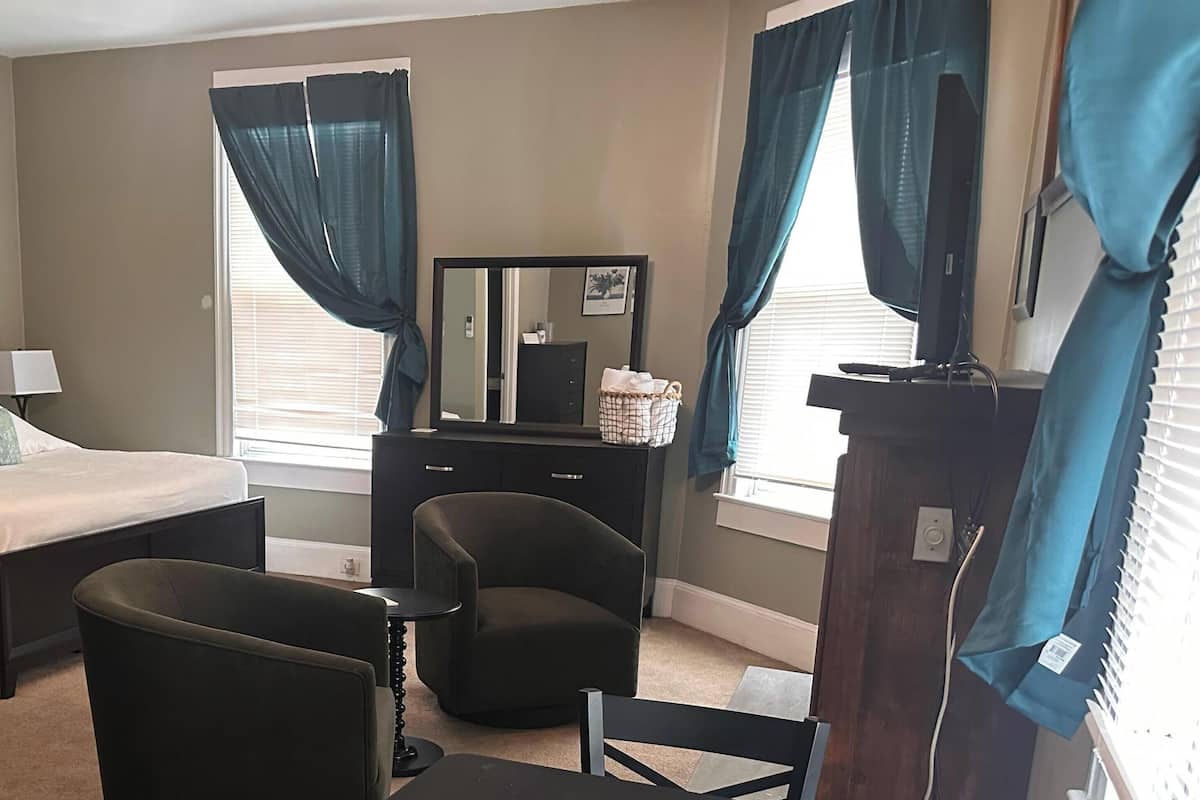 A bedroom with a bed, a chair, a dresser, a mirror, and a window with curtains.
