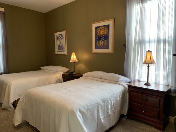 A hotel room with two beds, a nightstand with lamps, and two framed artworks on the wall. - The Hotel Belvidere (Hawley)