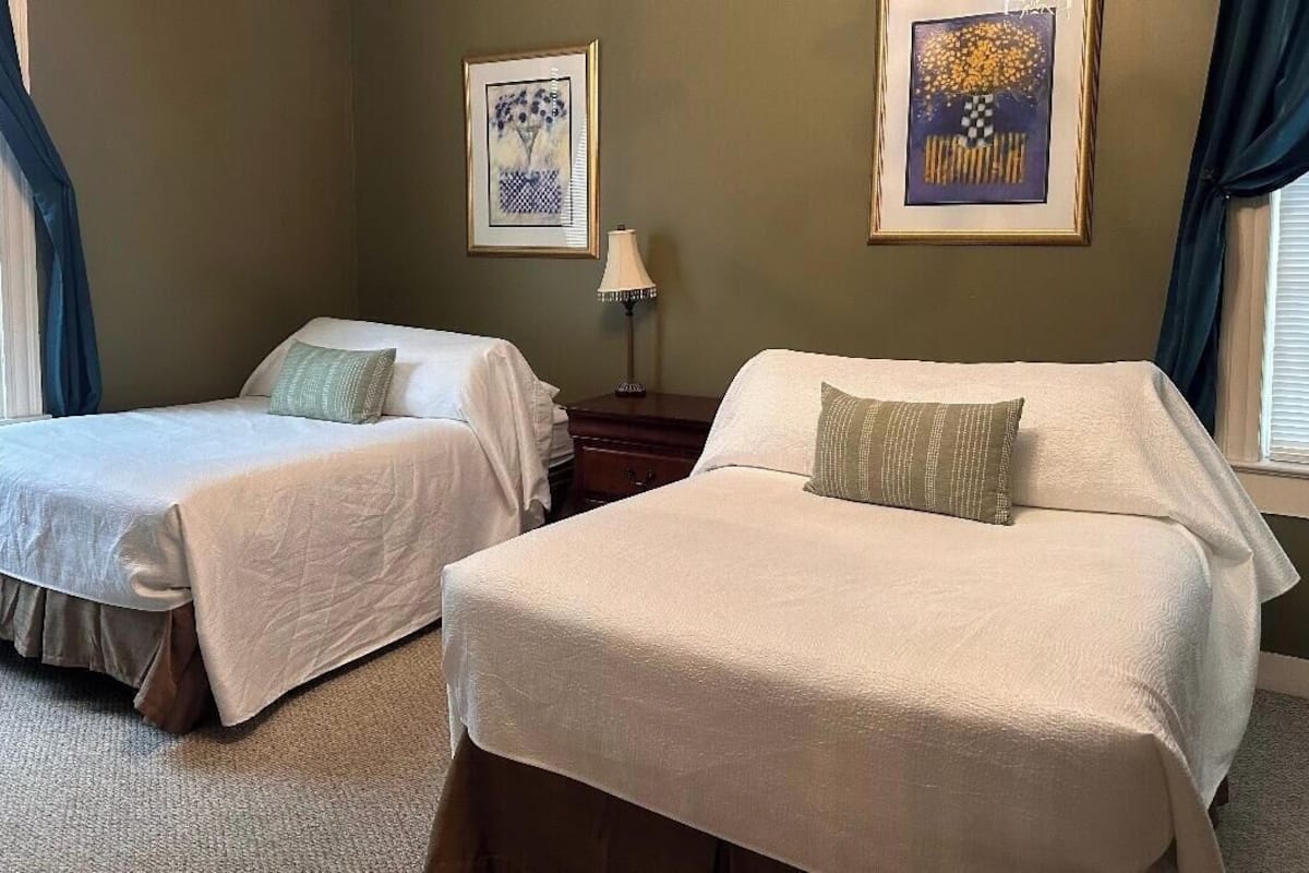 A room with two beds, a nightstand, and two framed pictures on the wall.