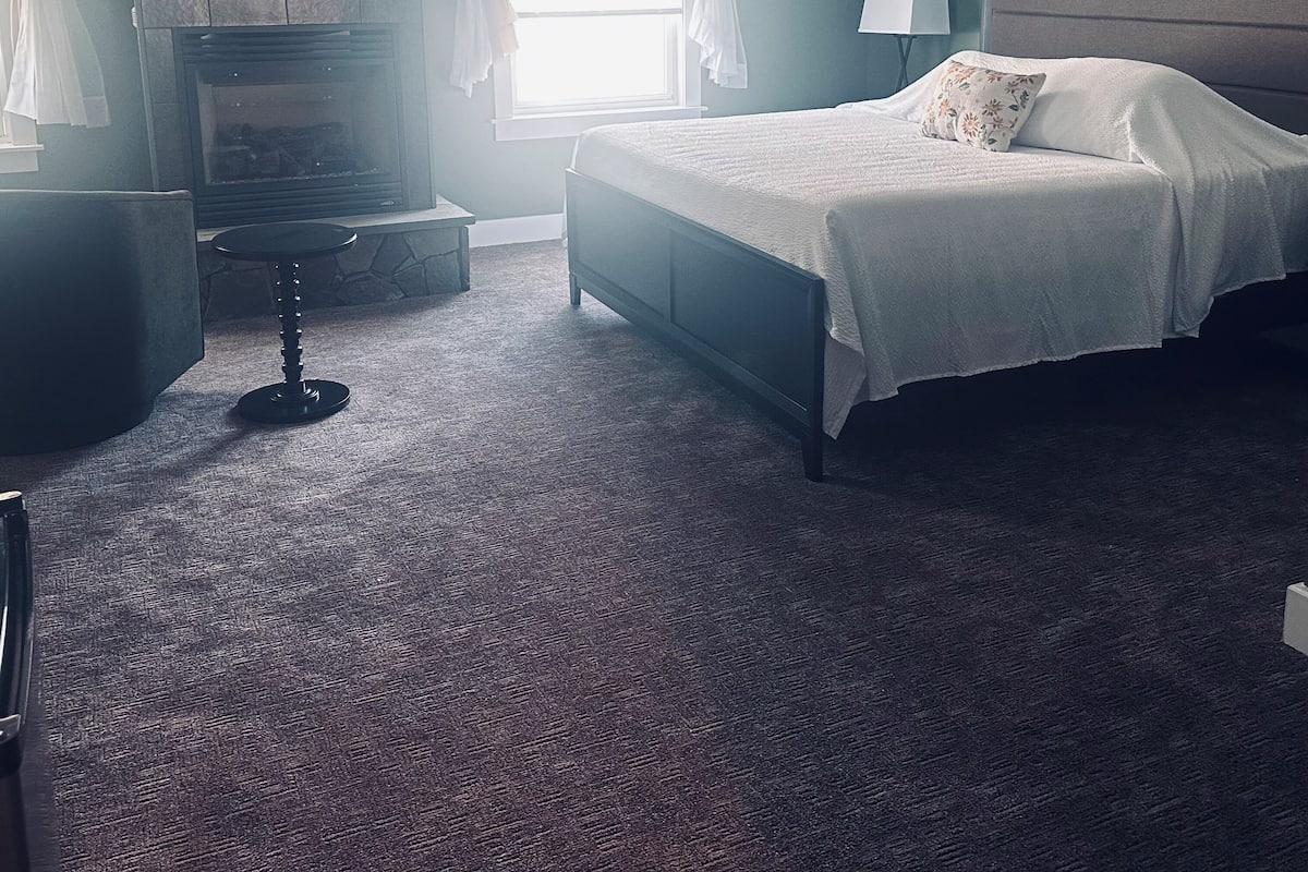 A bedroom with a bed, a fireplace, a chandelier, and a window with curtains.