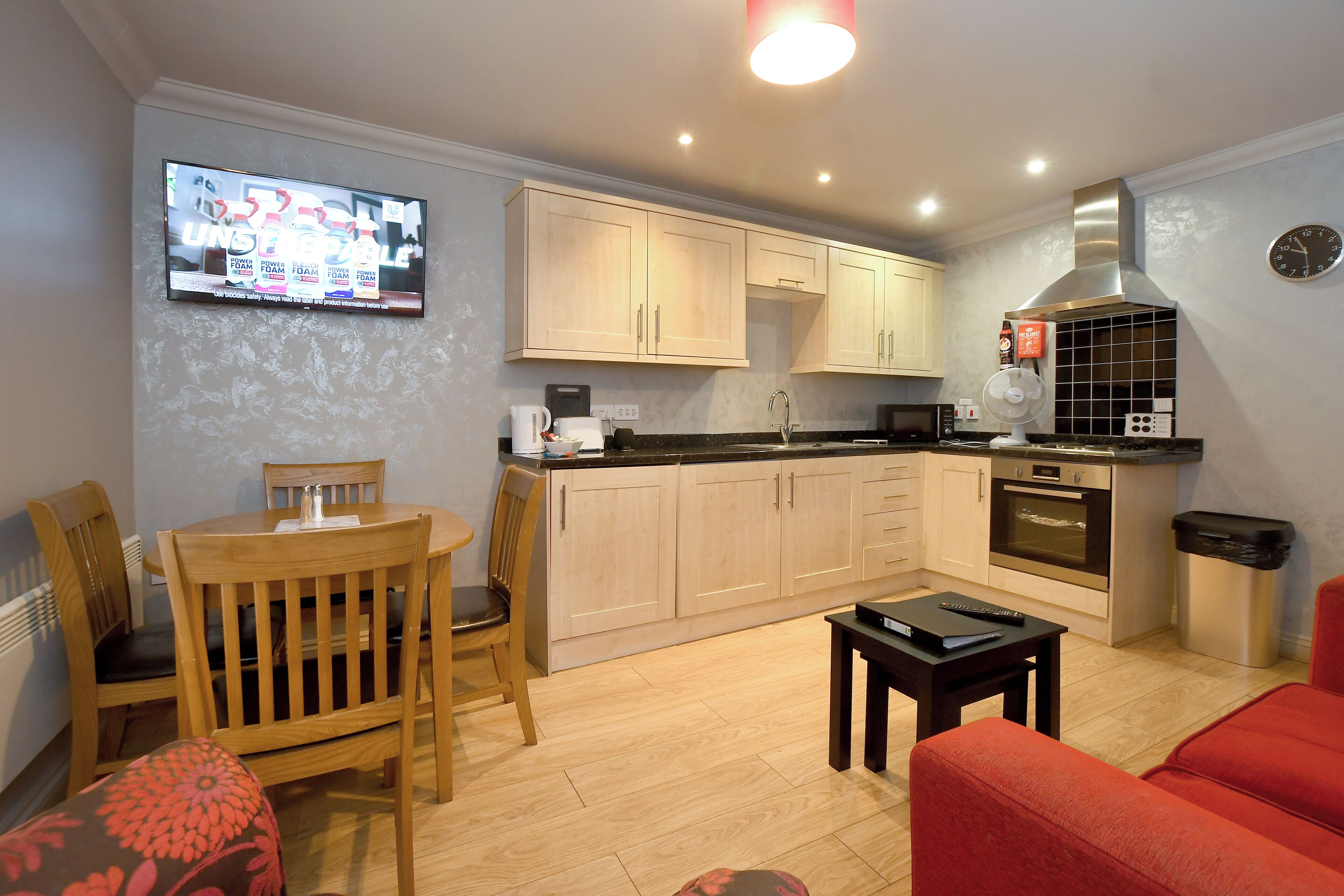 A compact living space with a dining area, kitchenette, and a television mounted on the wall.