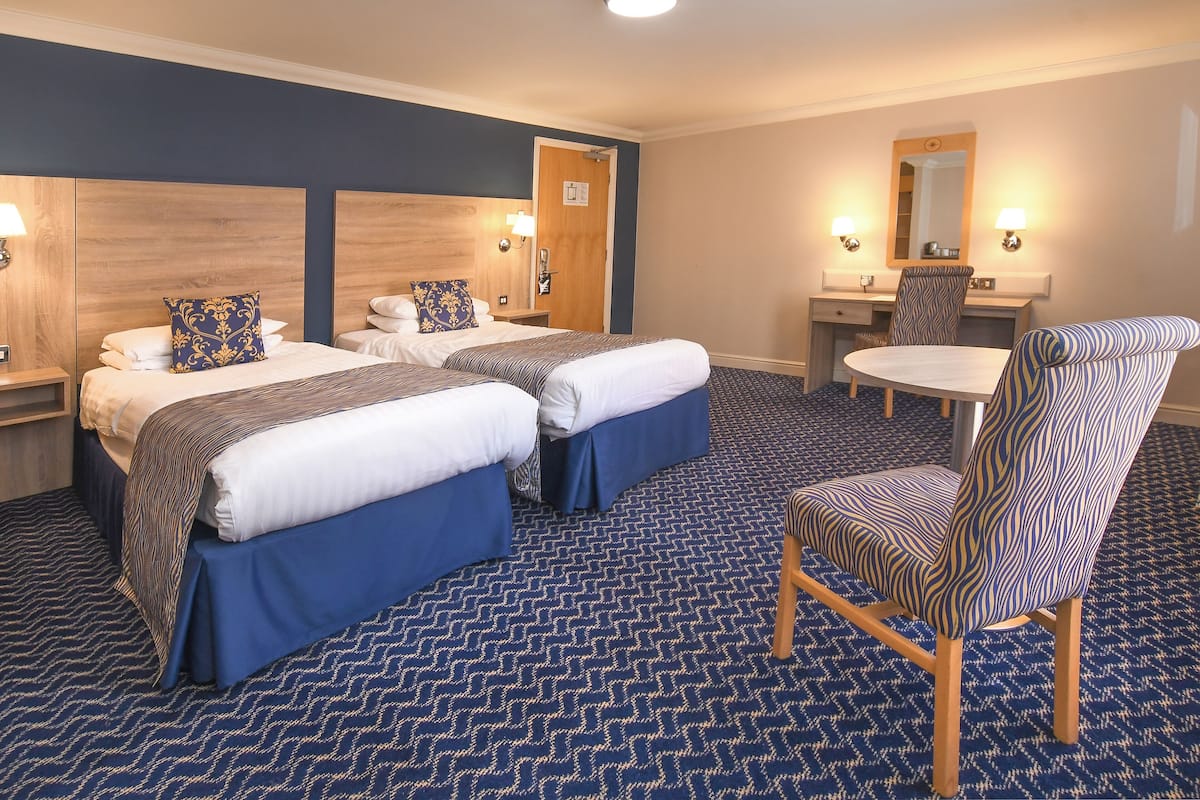 Habitación de hotel con dos camas, un escritorio, una silla y una mesita redonda.