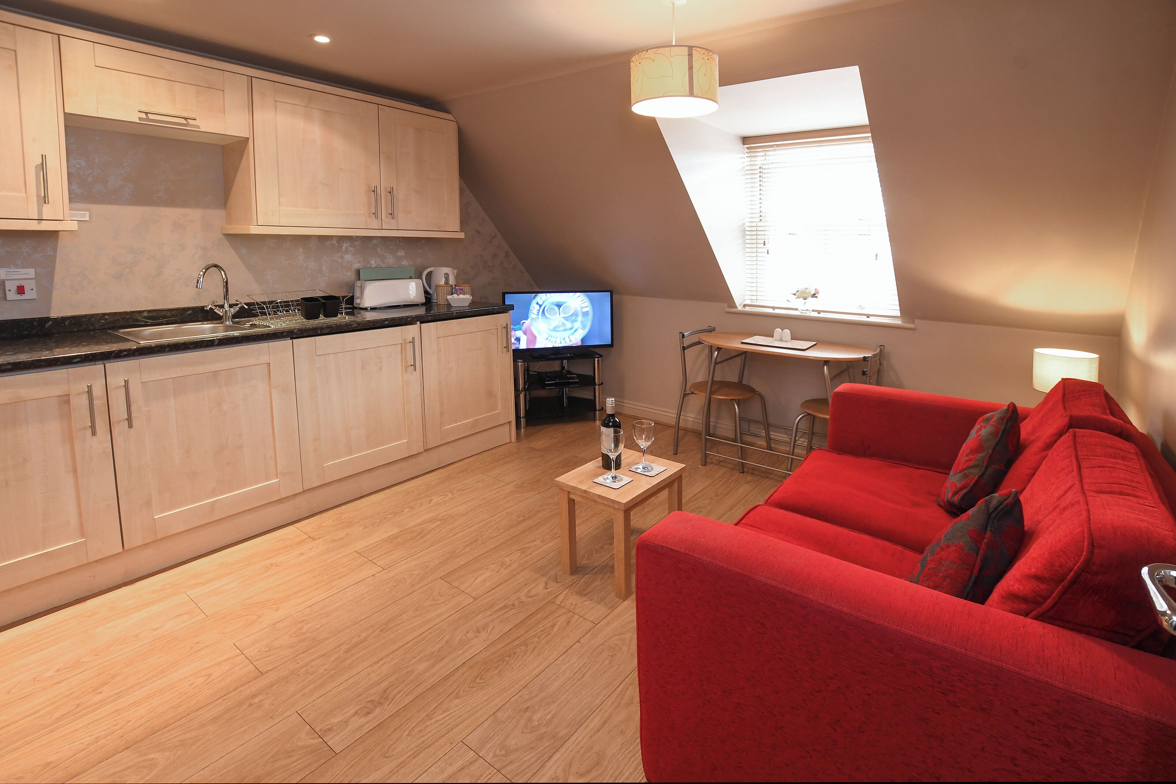 A modern kitchen with wooden cabinets, a countertop, and a dining area with a red sofa and a small table.