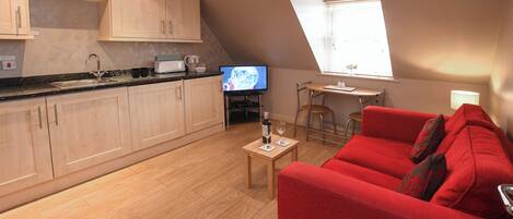 A modern kitchen with wooden cabinets, a countertop, and a dining area with a red sofa and a small table.