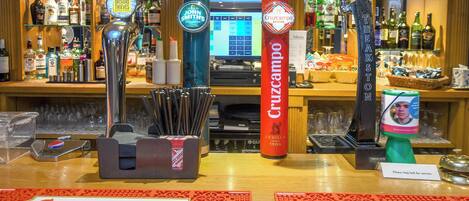 Zona de bar con varias cañas de cerveza, incluyendo marcas como John Smith's y Cruzcampo. También se observan varias botellas y vasos en estanterías al fondo.