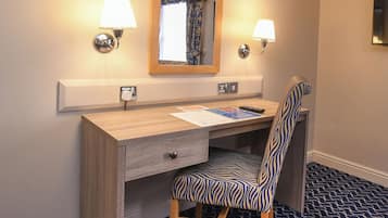 A hotel room with a wooden desk, a zebra-patterned chair, a mirror, two wall-mounted lamps, and a patterned carpet.