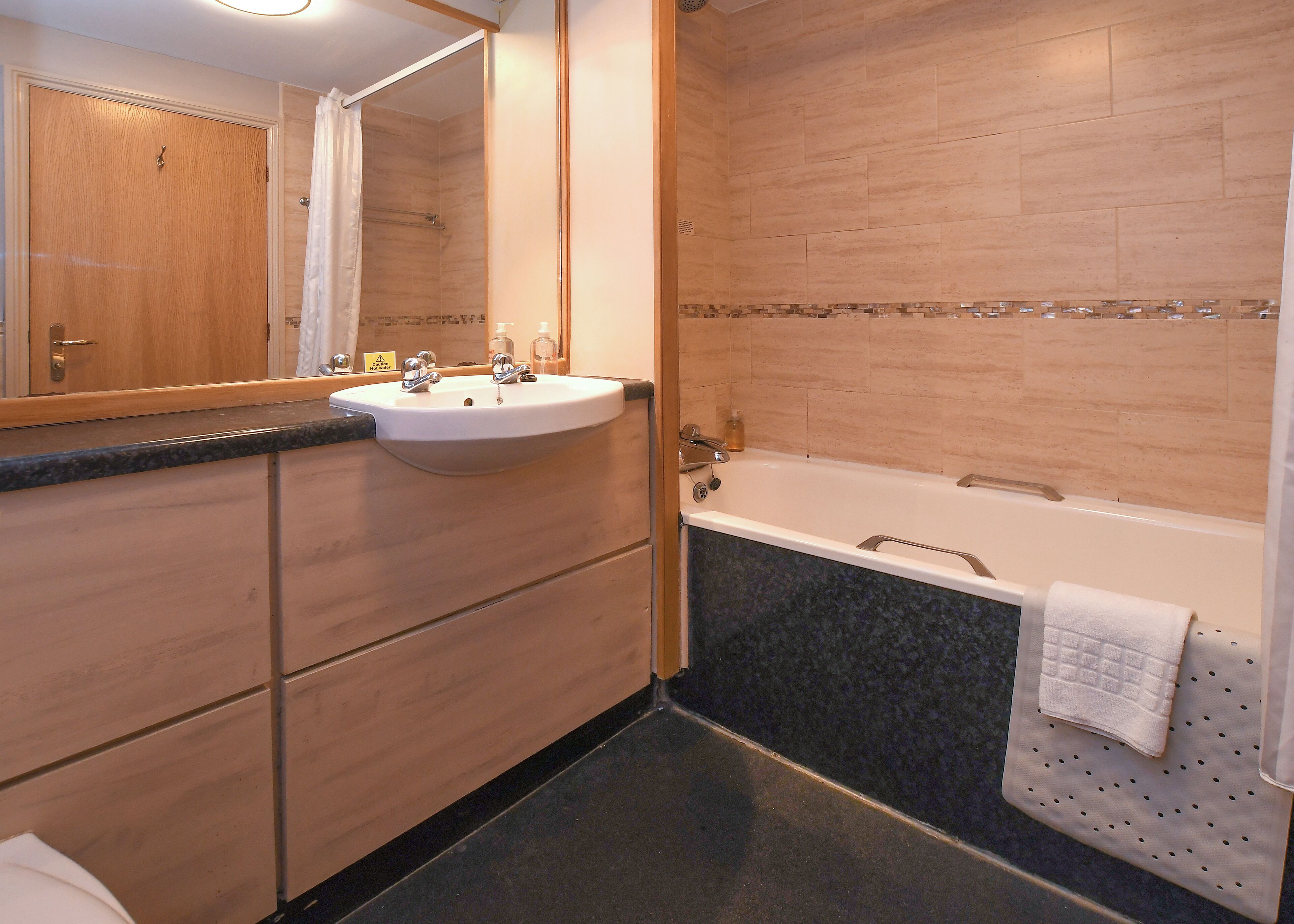 A bathroom with a wooden vanity, a sink, a mirror, a bathtub, and a towel rack.