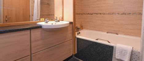 A bathroom with a wooden vanity, a sink, a mirror, a bathtub, and a towel rack.