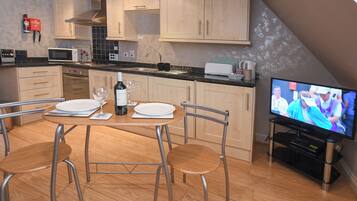A modern kitchen with wooden cabinets, a dining table with chairs, a TV, and a wine bottle.