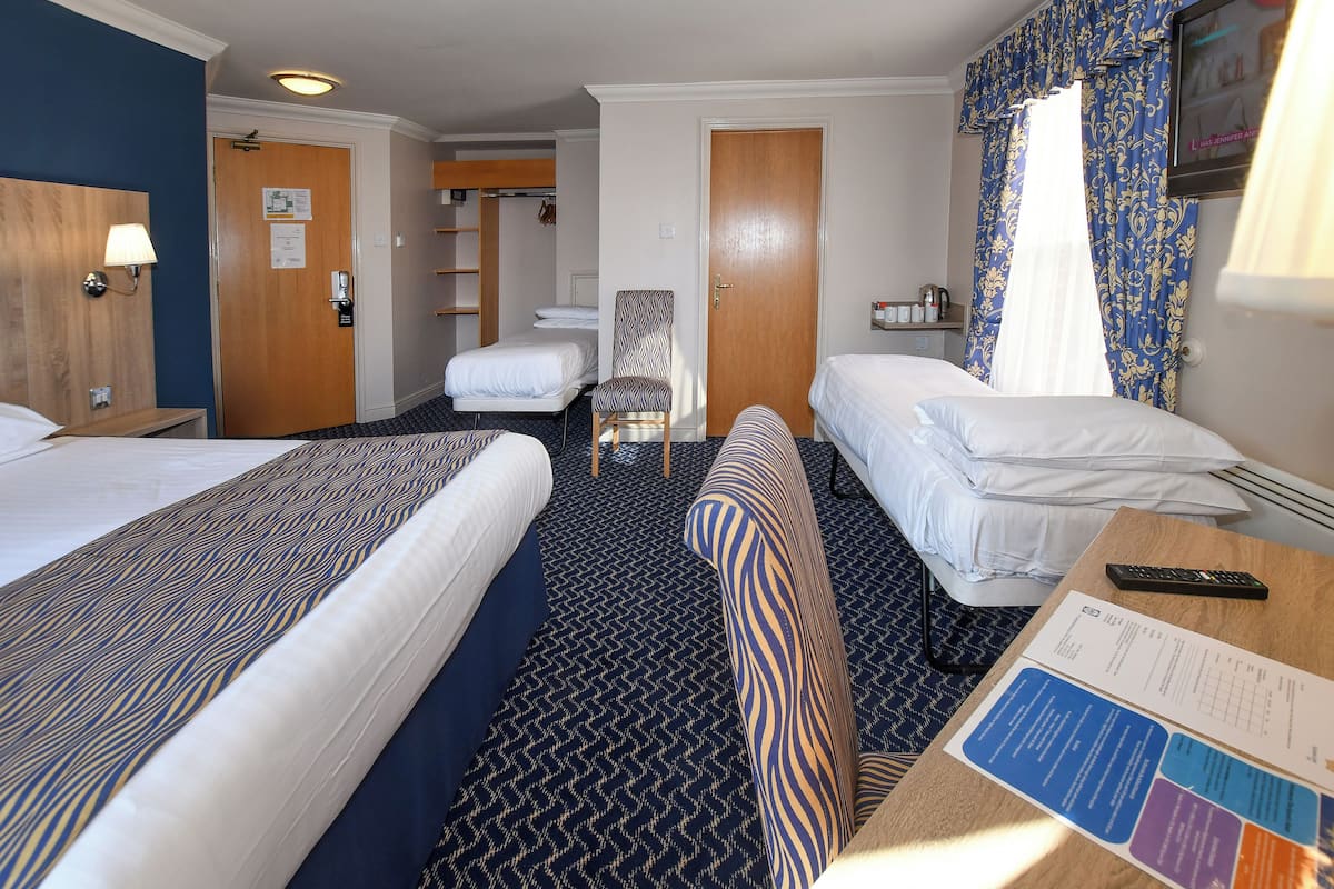 Habitación de hotel con dos camas, un escritorio con un control remoto, una silla, perchero y televisor en la pared.