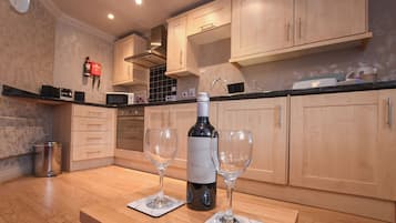 Una cocina con armarios de madera, microondas, una botella de vino y dos copas de vino sobre una encimera de mármol.