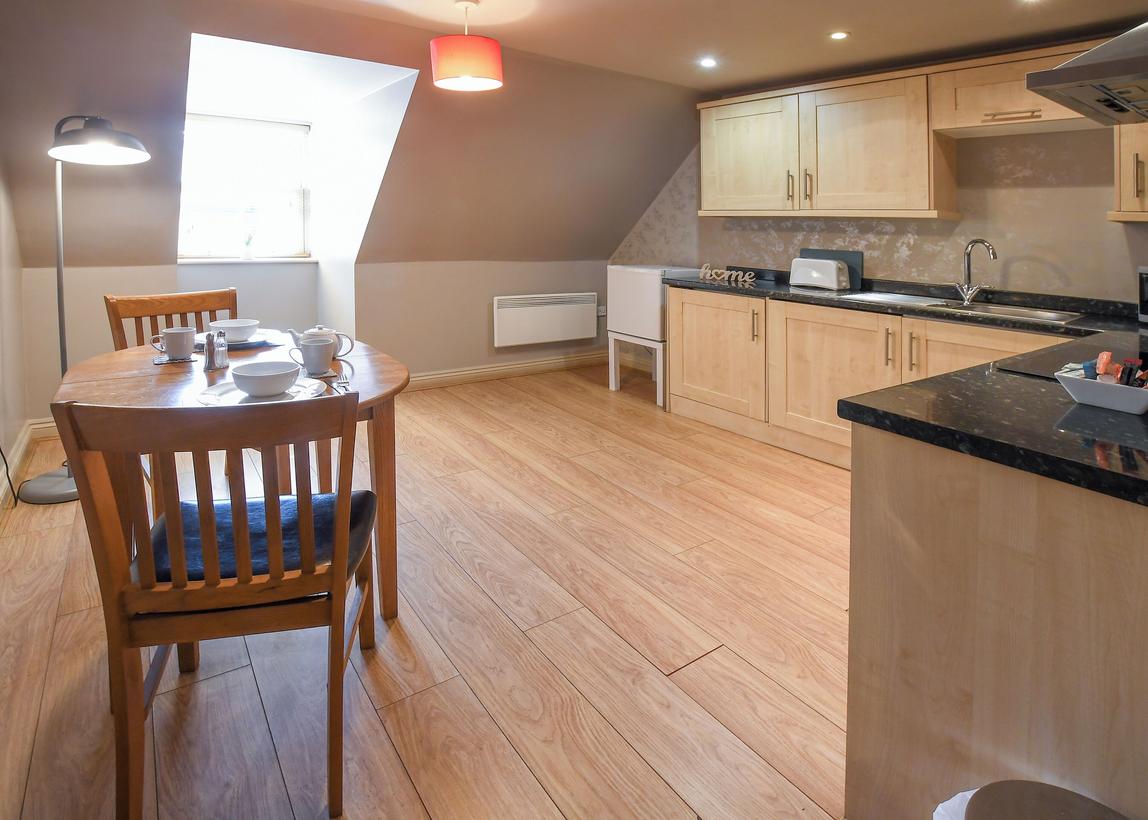Une cuisine moderne avec des meubles en bois, un plan de travail noir et un coin repas comprenant une table et des chaises.