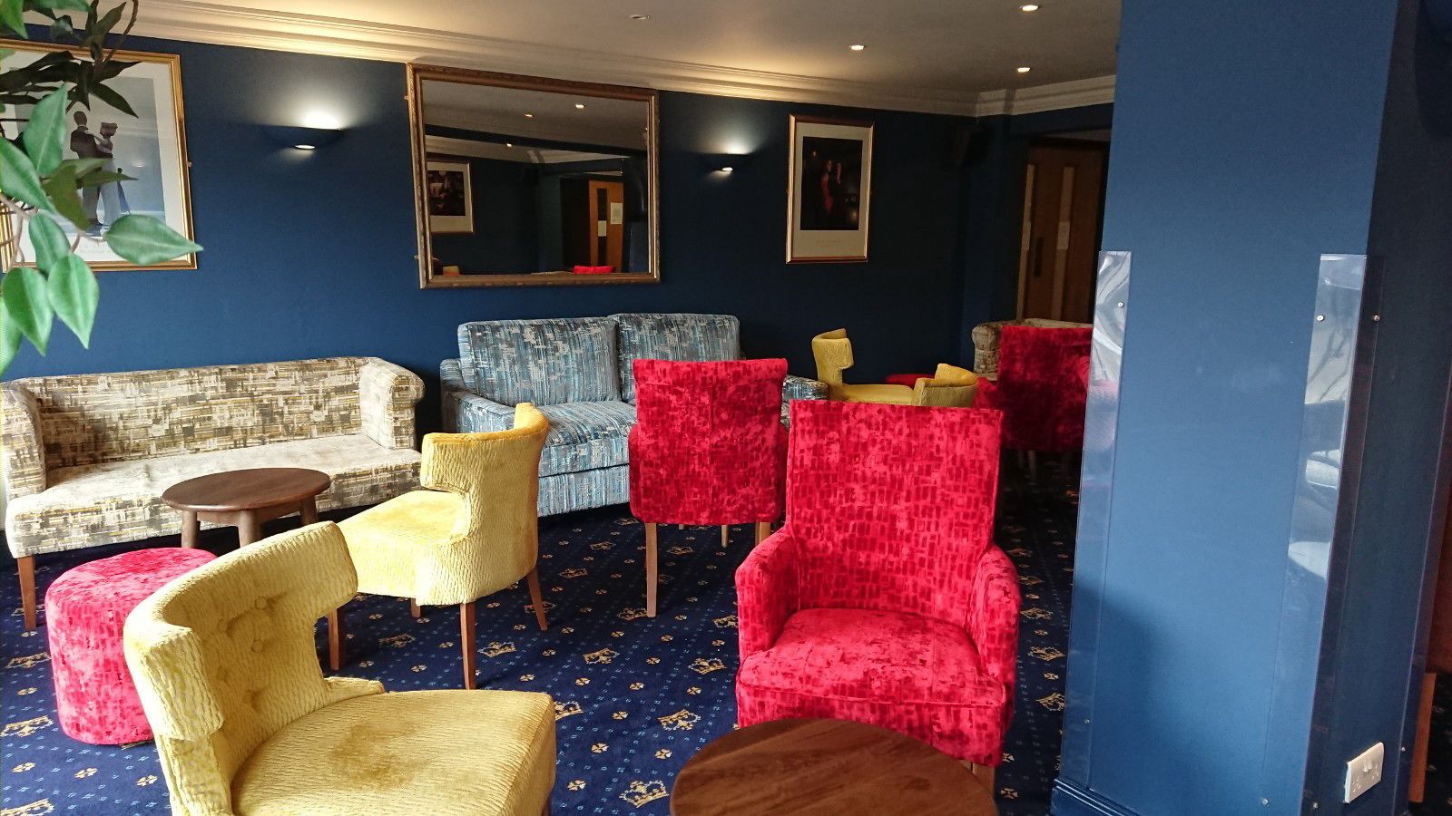 Una habitación con alfombra azul, un sofá, dos sillones, una mesita y un espejo en la pared.