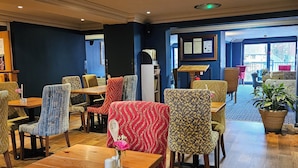 Un restaurante con mesas y sillas de madera, una pared azul y un ventanal grande.