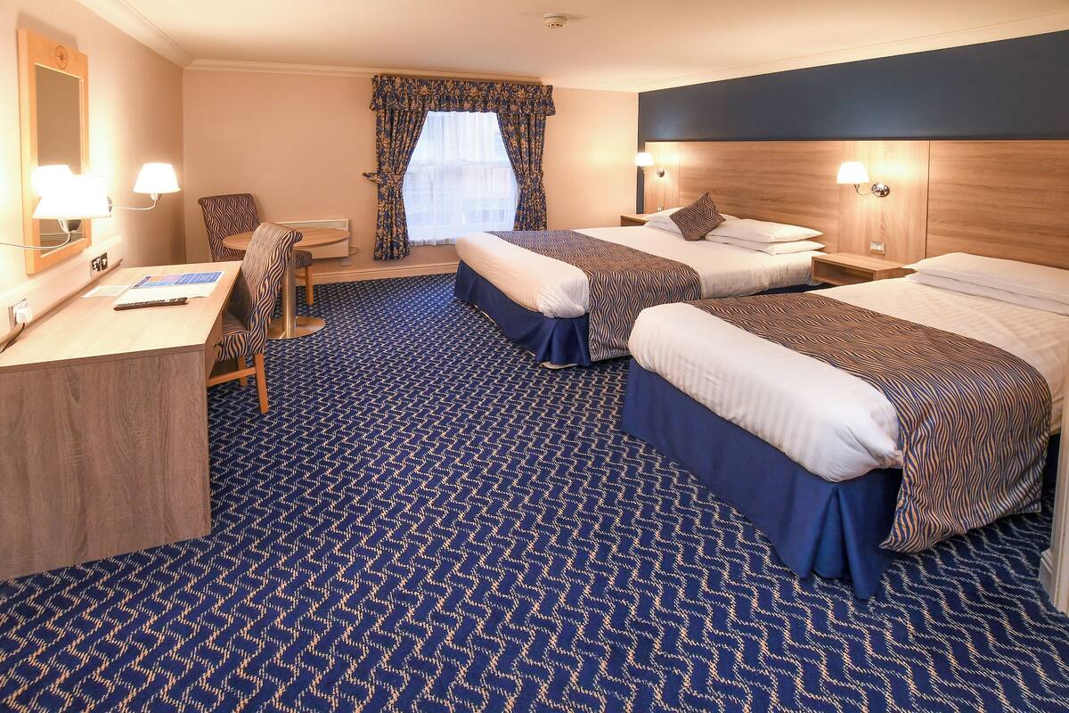 Una habitación de hotel con dos camas, un escritorio, una silla y una ventana con cortinas.