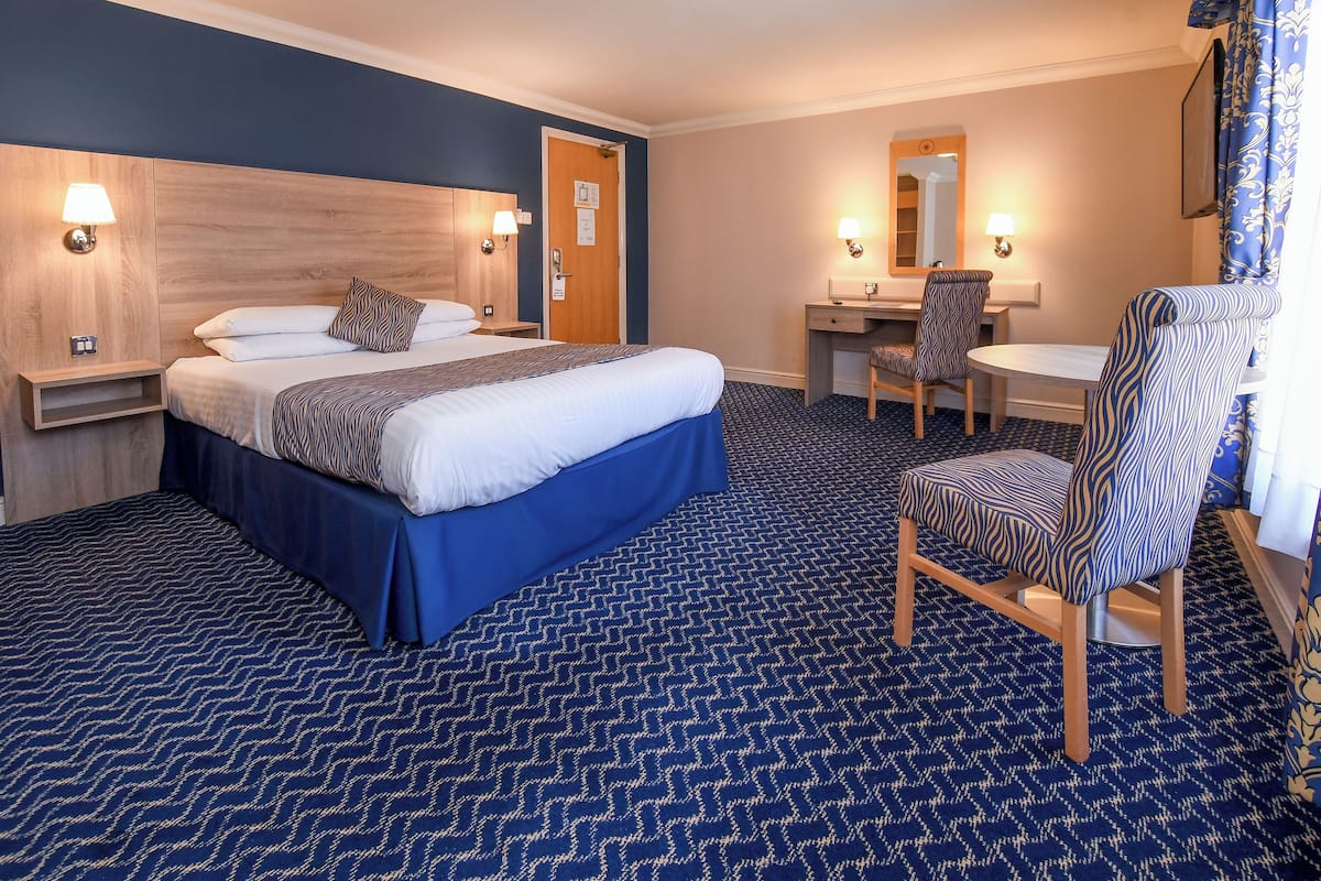 Una habitación de hotel con cama, escritorio, silla y espejo.