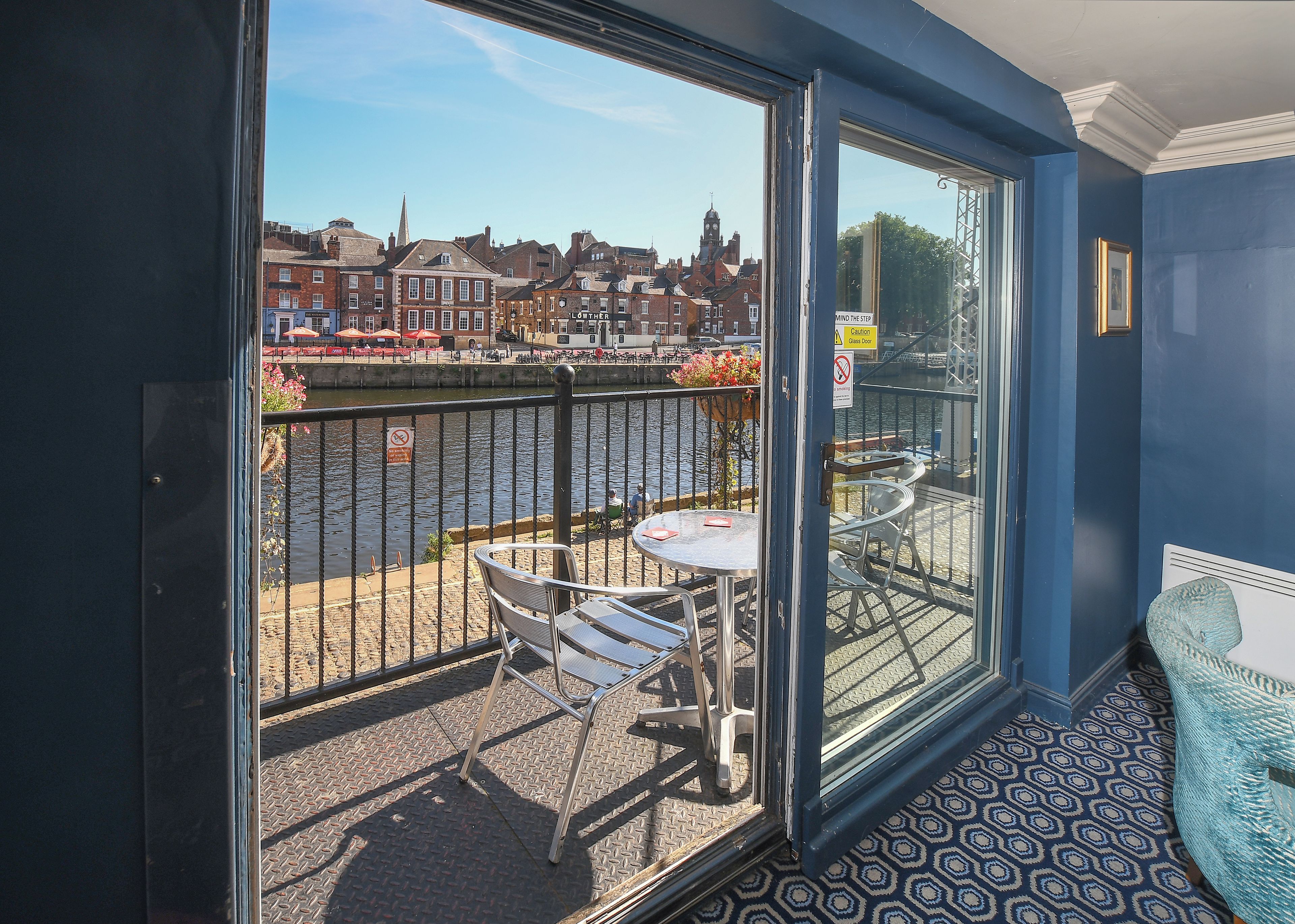 A balcony with a table and chairs, a view of a river, and buildings in the background.