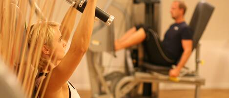 Un gimnasio con equipo de ejercicio, incluyendo una máquina de poleas y una máquina sentada.