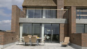 A modern building with a brick facade, large glass windows, and a covered patio area with outdoor furniture. - Enjoy Resorts Rømø (Rømø)