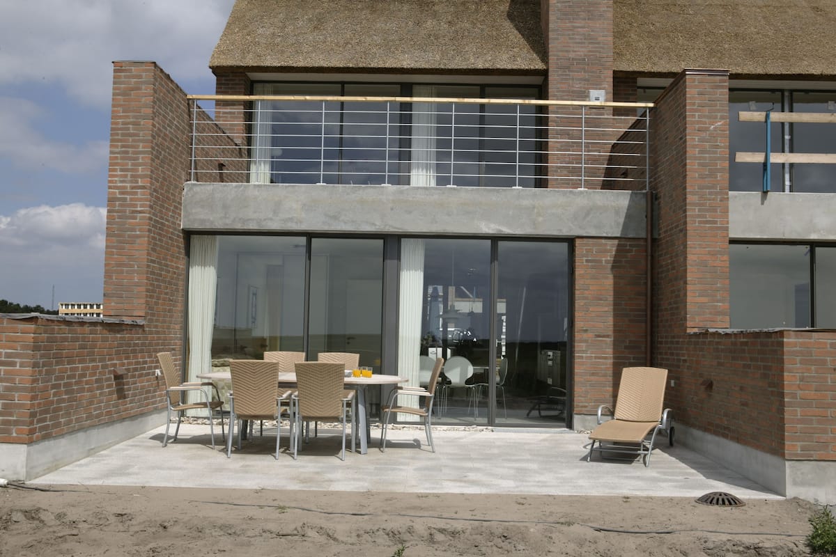 Un bâtiment moderne avec une façade en briques, de grandes fenêtres en verre et un patio couvert aménagé avec du mobilier d’extérieur.