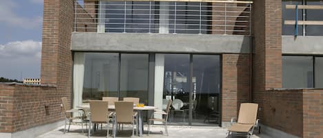 Un edificio moderno con fachada de ladrillo, amplios ventanales y un patio cubierto con mobiliario exterior.