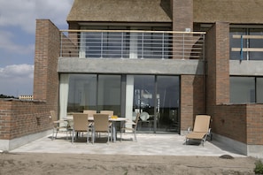 A modern building with a brick facade, large glass windows, and a covered patio area with outdoor furniture. - Enjoy Resorts Rømø (Rømø)