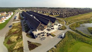An aerial view of a residential area with modern houses, a large building with a sloped roof, and a parking area. - Enjoy Resorts Rømø (Rømø)