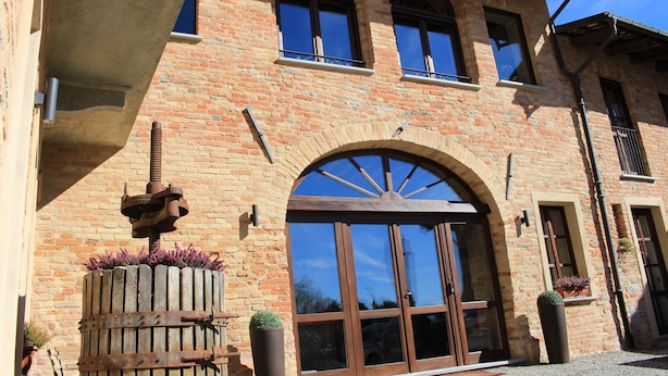 A brick building with a large arched entrance, windows, and potted plants. - Dimora Cortese (Castagnole delle Lanze)
