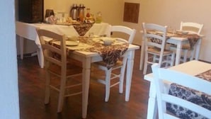 A dining area with white chairs and a table set for four. There is a chandelier above the table, and a cabinet with various items on the left side. - Dimora Cortese (Castagnole delle Lanze)