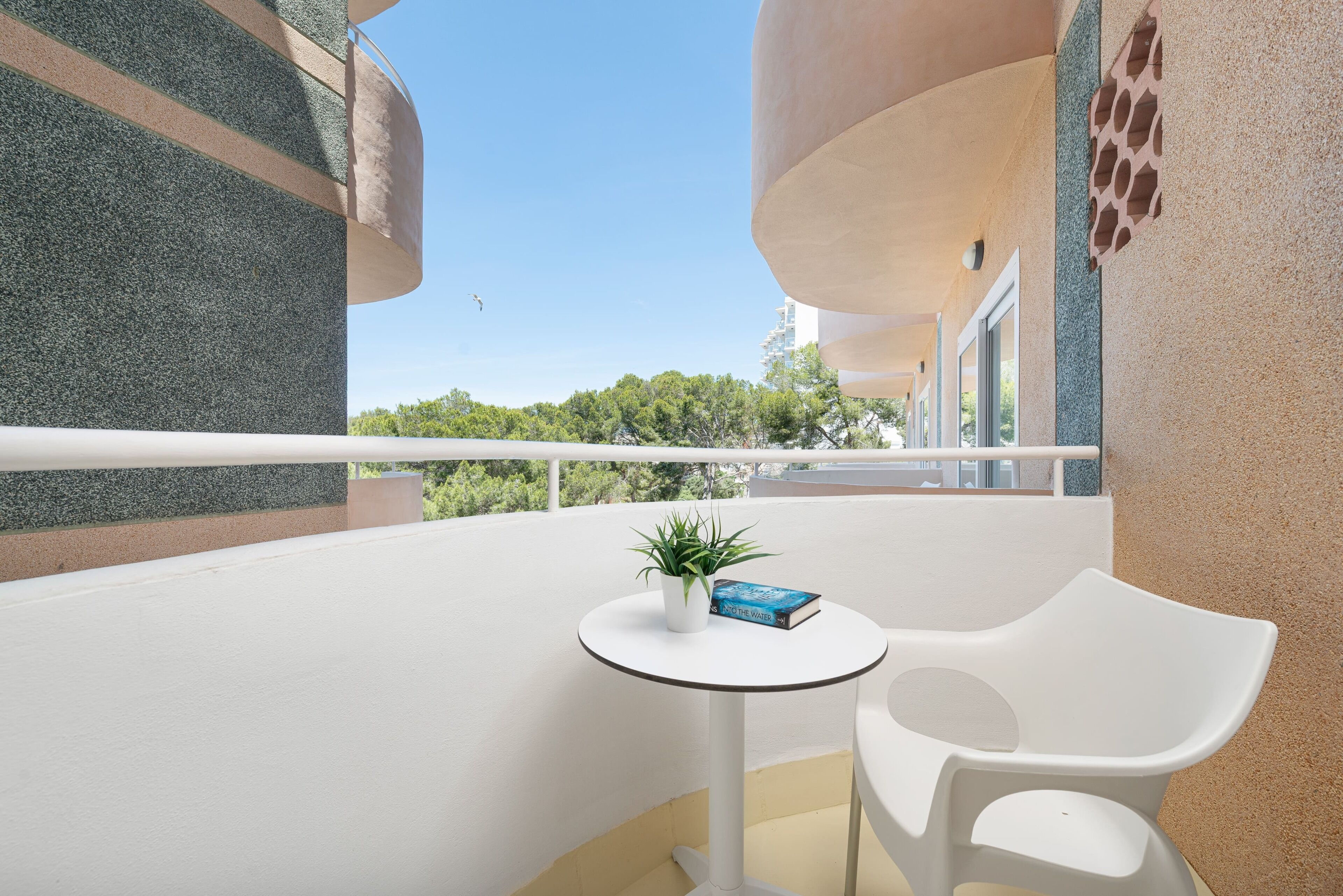 Un balcon avec une chaise blanche, une petite table et un pot de fleurs.