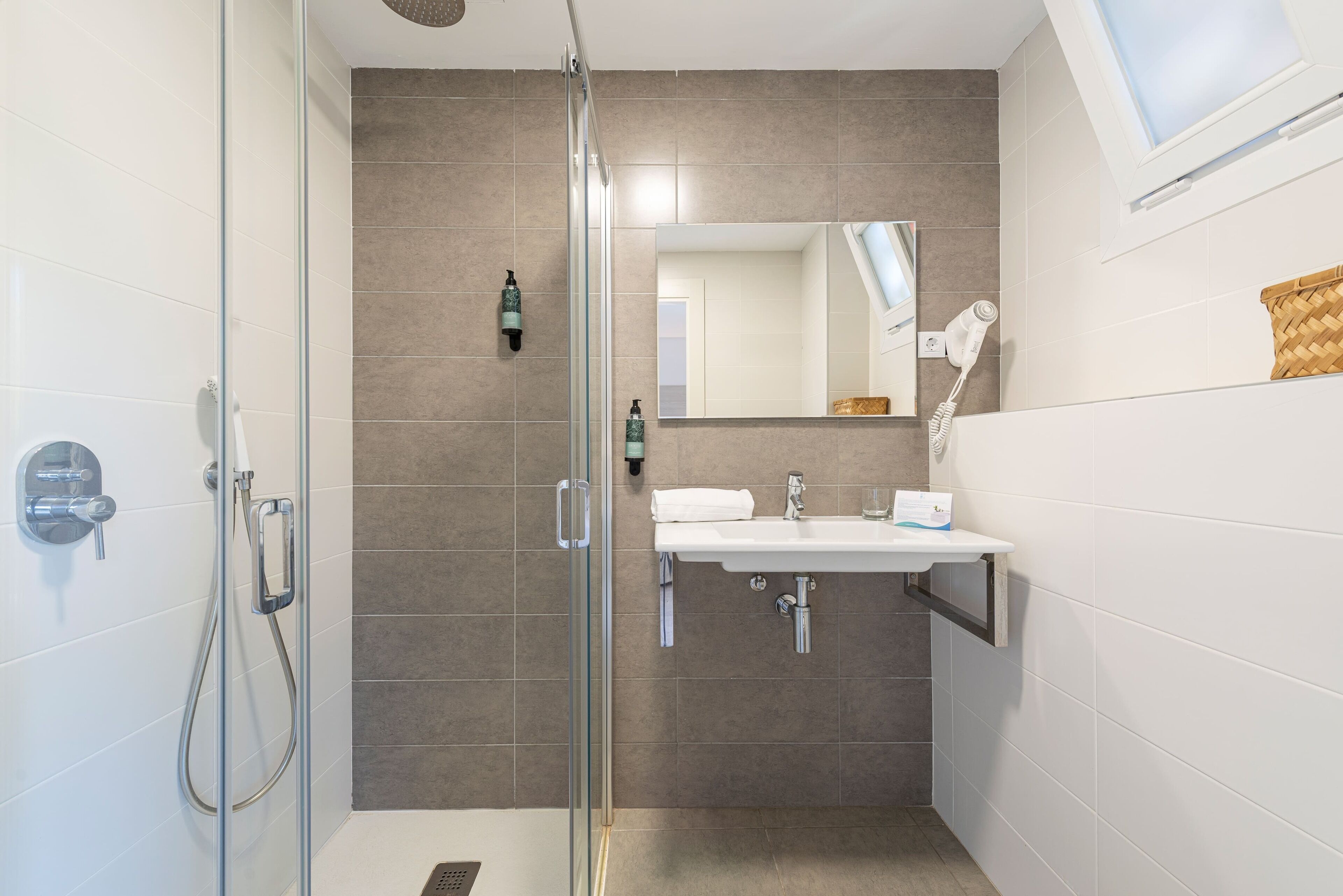 A modern bathroom with a glass shower enclosure, a white sink, and a hairdryer mounted on the wall.