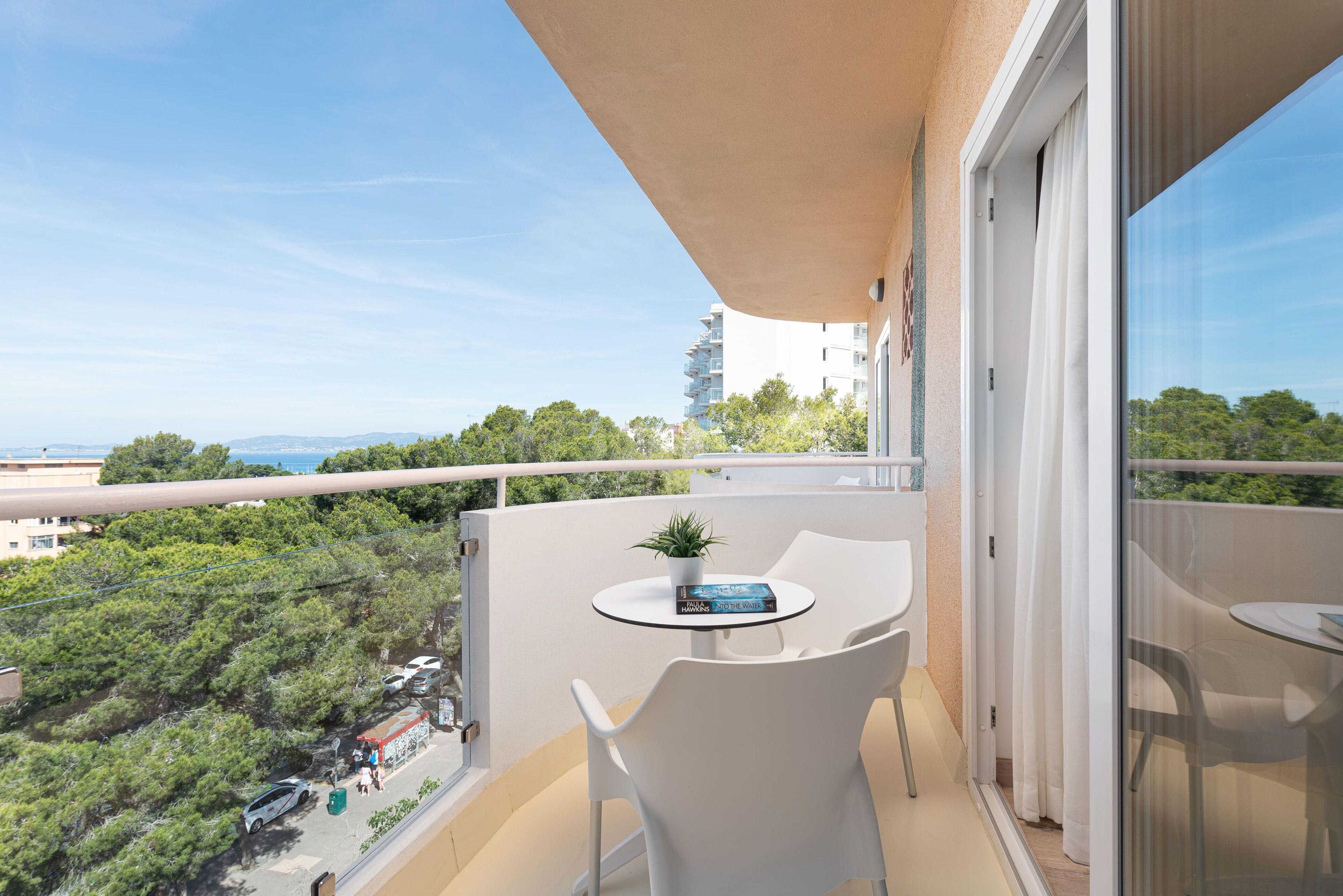 Un balcón con mesa y sillas, con vistas a un paisaje urbano con árboles y edificios.