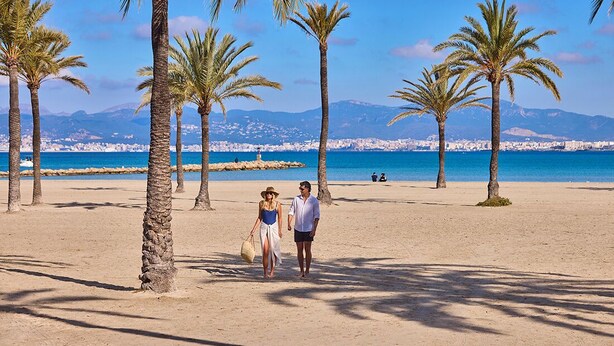 A beach with palm trees and a clear view of the sea and mountains in the background. - Welikehotel Fenix (Llucmajor)