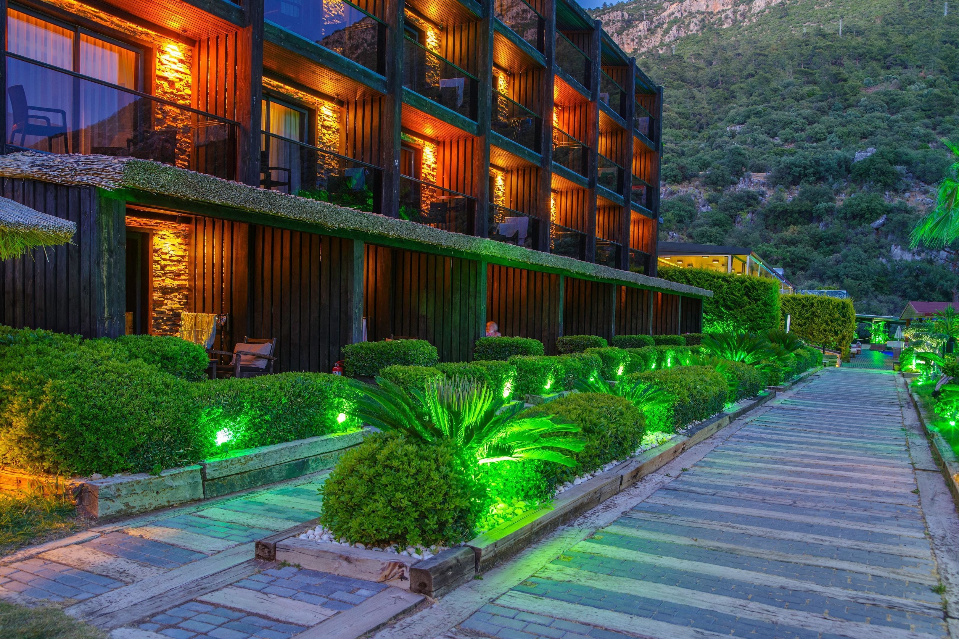 Un hotel moderno con varios balcones, un camino bien iluminado y setos cuidadosamente podados.