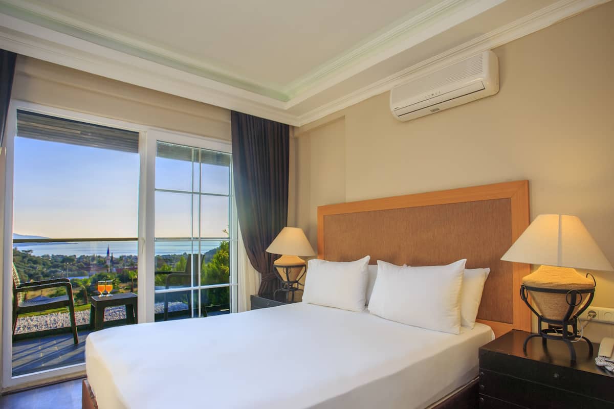A hotel room with a large bed, two bedside lamps, a phone, and a view of a cityscape through a large window.