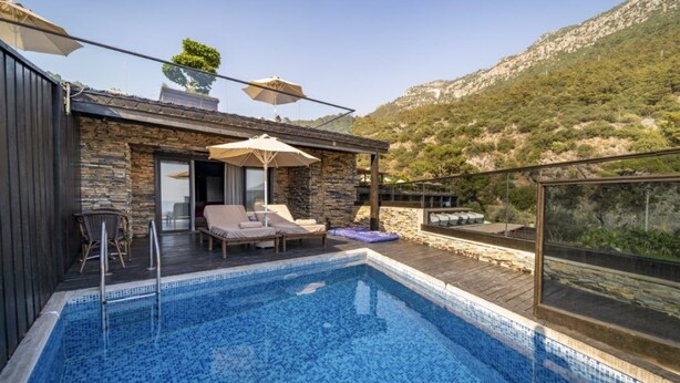 A rooftop pool with lounge chairs and umbrellas, surrounded by stone walls and a view of a mountainous landscape. - Manaspark Deluxe Hotel (Fethiye)
